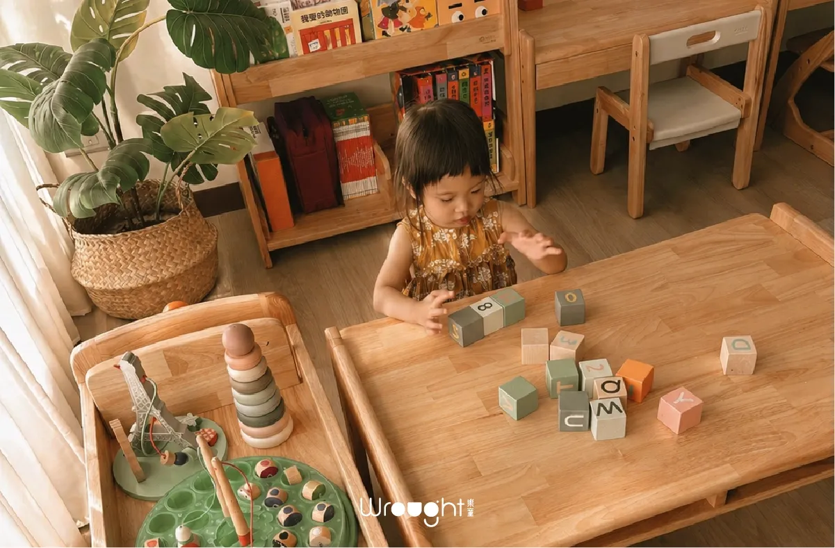 孩子3C使用時間-幼兒在原木兒童桌前專注玩字母積木,背景有書架與玩具,展現實體遊戲環境對幼兒發展的重要性
